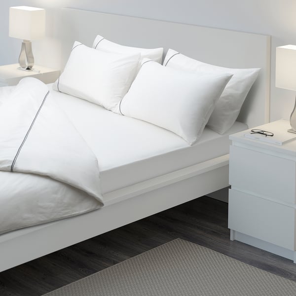 A neatly made bed with crisp white sheets. The fitted sheet has elastic edges, perfectly fitting a thick mattress.
