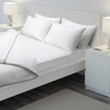 A neatly made bed with crisp white sheets. The fitted sheet has elastic edges, perfectly fitting a thick mattress.