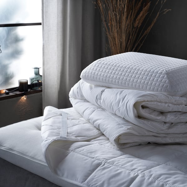 Stack of white STRANDMOLKE duvet and pillows on bed - soft, quilted cotton and polyester.