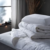 Stack of white STRANDMOLKE duvet and pillows on bed - soft, quilted cotton and polyester.