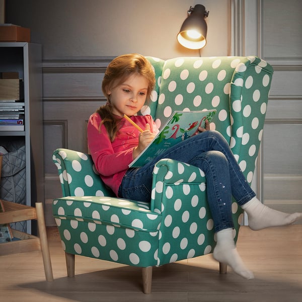 Girl in turquoise polka dot chair reading book.