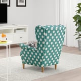 Cat resting on a teal polka dot STRANDMON armchair in a cozy living room.