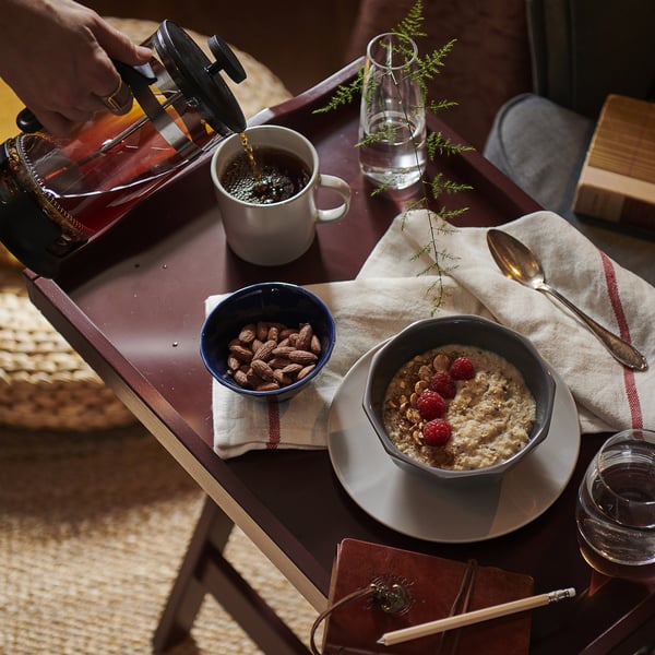 Person pouring coffee near breakfast items, including oats with berries and almonds in bowls, on a table with a notebook and pencil.