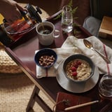 Person pouring coffee near breakfast items, including oats with berries and almonds in bowls, on a table with a notebook and pencil.
