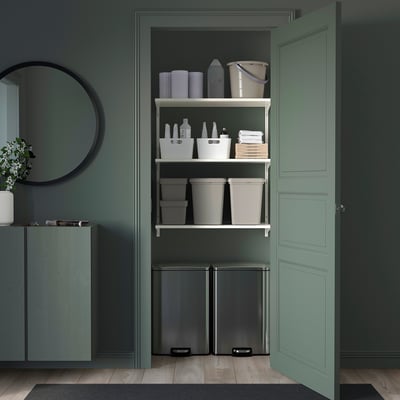 Neat, organized shelf unit in white metal with plastic bins, bottles, and cleaning tools; fits under green counter within a decorations room.
