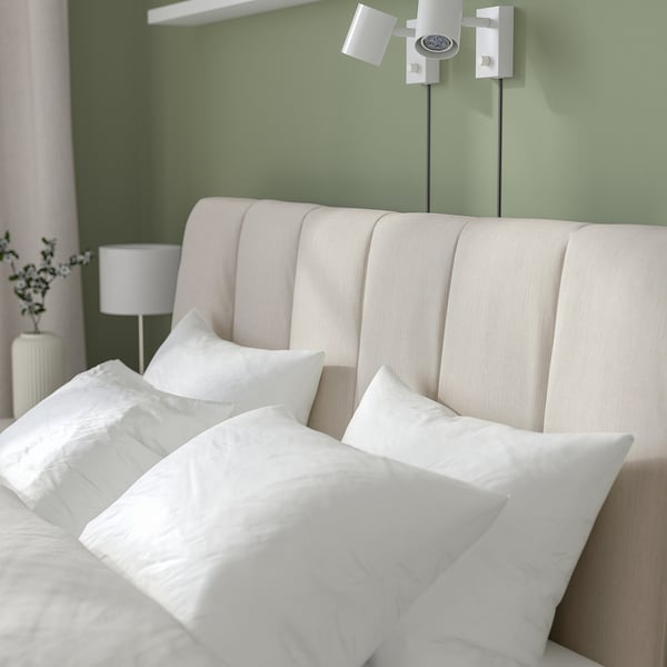 Modern adjustable bed with padded headboard, striped beige fabric, bedside lamps, and vase.