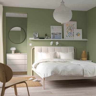 Modern bedroom with TÄLLÅSEN white bed, matching nightstand, and wall art. Soft green walls and wooden floor.