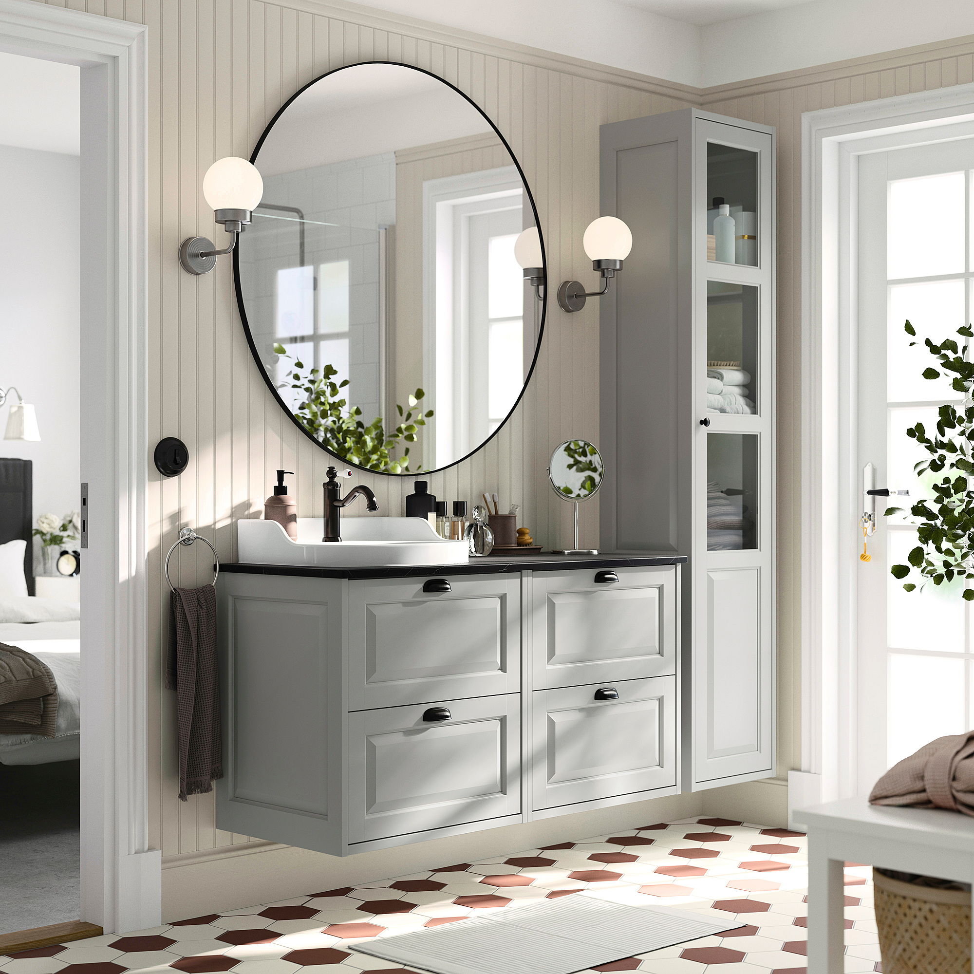 Modern grey bathroom vanity with large round mirror. Grey cabinets, black fixtures, patterned floor. Spacious.