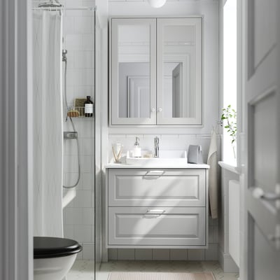 Modern white bathroom with TÄNNFORSEN light grey cabinet, semi-recessed sink, mirror, and shower. Clean and spacious design.