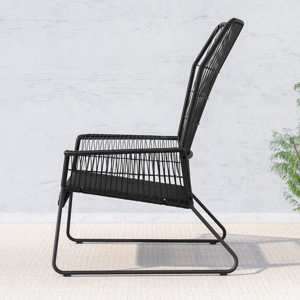 Black wicker outdoor chair with curved back and seat, set against a light wall. Minimalist design, comfortable for relaxing.
