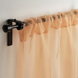 Peach sheer curtains hang from black rod, diffusing light, offering privacy by day.