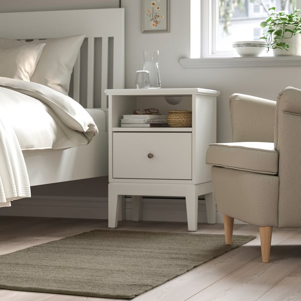 Bedroom with TIDTABELL nightstand, white bed, armchair, grey rug, cozy minimalist design.