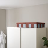 Two TJENA boxes, maroon with blue stripes, sit atop a white cabinet, larger than the white towel hanging nearby.