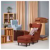 Two colorful armchairs with cushions in room, light beige curtains, bookshelves with plants and boxes.