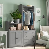 Modern bedroom with gray TJOG storage unit, clothes, plant, and chair.