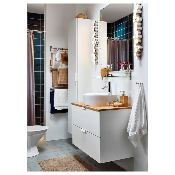 Modern bathroom with white sink vanity, light wood counter, gray-tiled shower, and hanging towels.