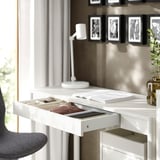 A white desk with an open drawer displaying contents.