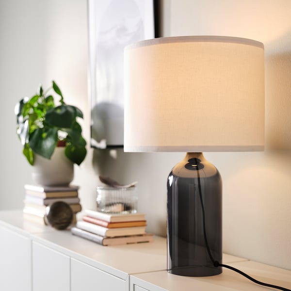 TONVIS table lamp with smoked glass base and beige shade, on white surface with books and plant.