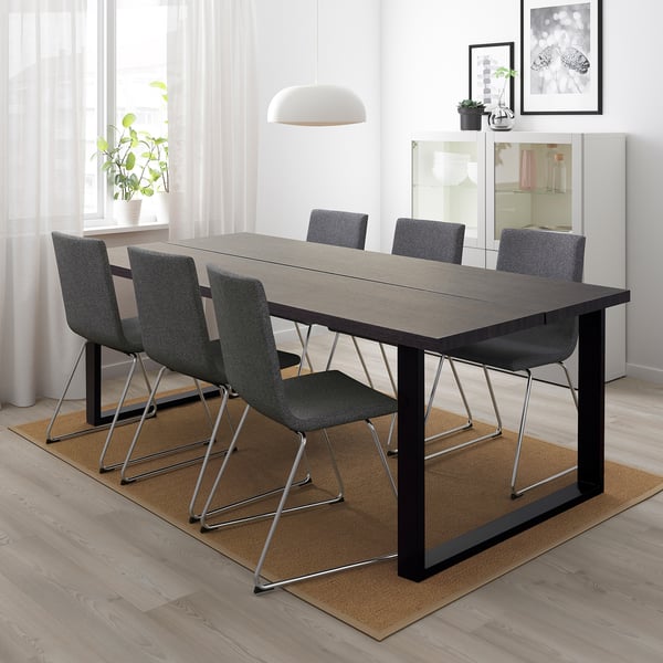 A TRANEBO rectangular dining table with 6 grey chairs on a beige rug, large window, art, pendant light.