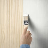 A hand uses a brush to paint a wooden surface with TRIXIG, a water-based, semi-matte indoor furniture paint.