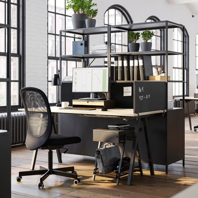 Modern office setup with TROTTEN black metal double-sided cabinet, computer desk, chair, and shelves with plants.