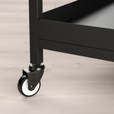 Modern black metal trolley with wheels on wooden floor. Robust construction for stability and ease of movement.