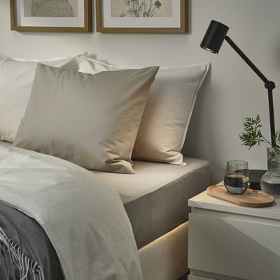 Bed with gray ULLVIDE pillowcases & blanket, small nightstand, lamp, glass.
