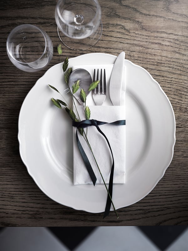 Rustic place setting: UPPLAGA plate, black napkin, greenery, silverware, glass.
