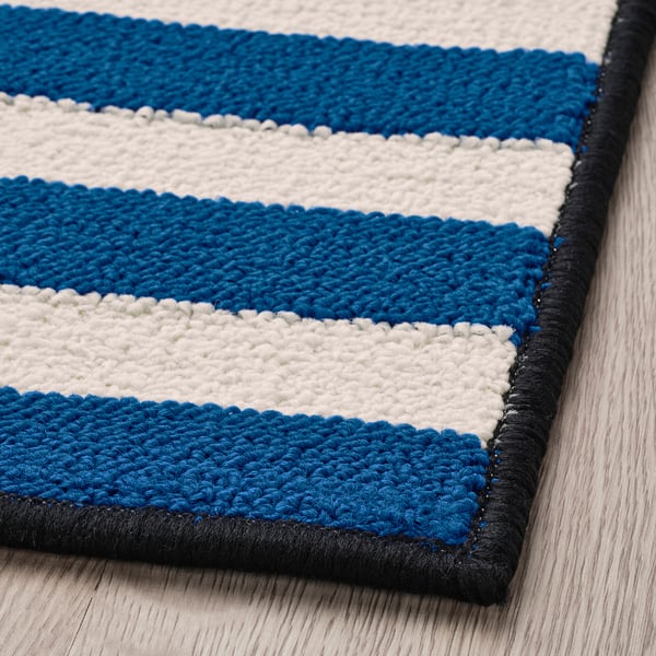 Striped blue and white rug with black border on wooden floor.