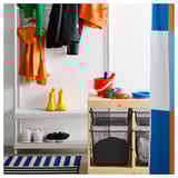 Organized entryway with hanging jackets, yellow boots, white sneakers, black mesh storage, colorful buckets, and striped rug.