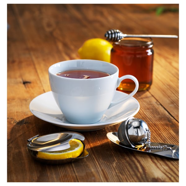 Tea on saucer with honey, lemon, and strainer.