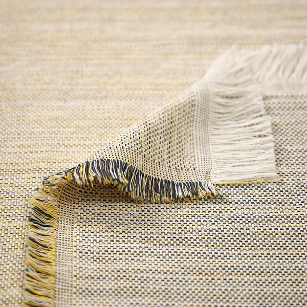 This image shows a close-up of a woven throw with colorful fringes, made from recycled materials.