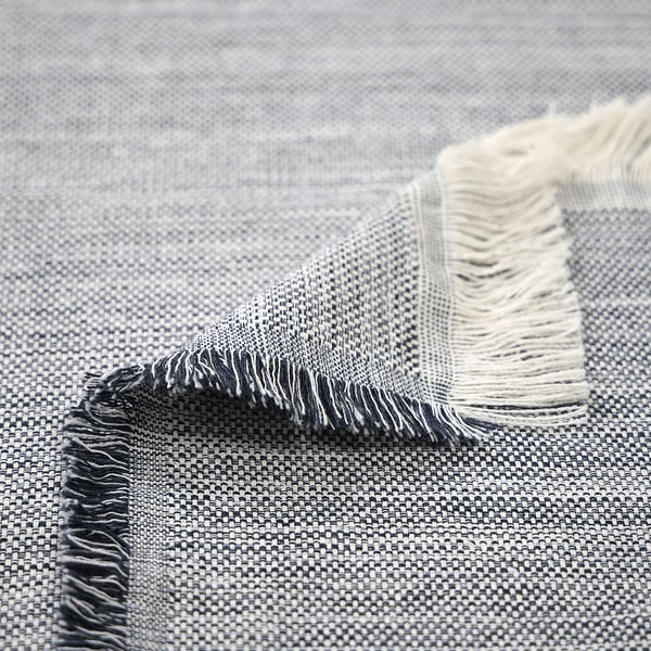 Textured, woven throw with fringes, featuring light and dark shades. High-quality, recycled fibers, visible in intricate weave.