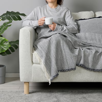 Person enjoying tea on light sofa with VÄXELBRUK blanket