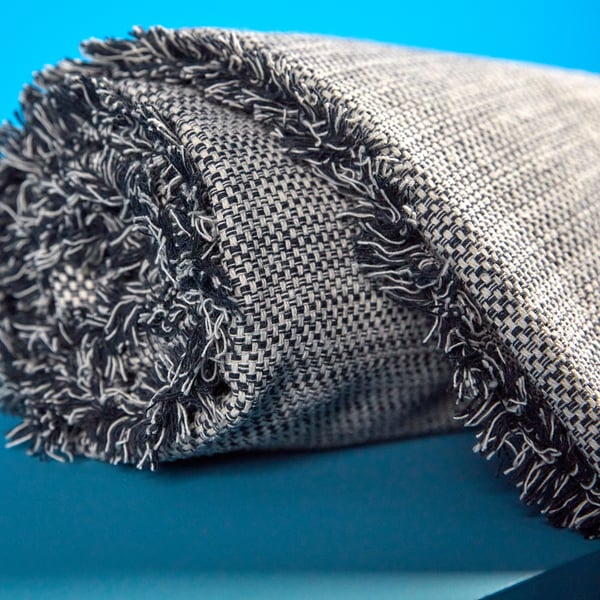 Folded gray throw with fringe on teal background. Soft, recycled fabric with varied texture.