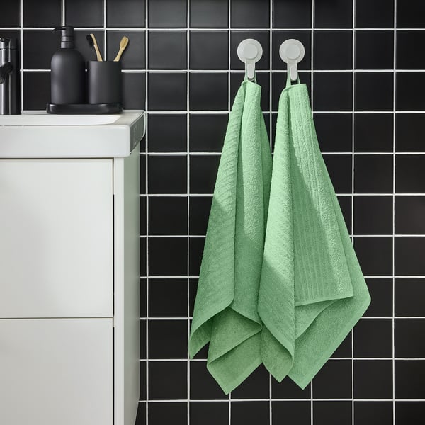Modern bathroom with dark tiles, white cabinet, & green VÅGSJÖN towels. Light & absorbent, they brighten the space.