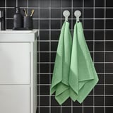 Modern bathroom with dark tiles, white cabinet, & green VÅGSJÖN towels. Light & absorbent, they brighten the space.