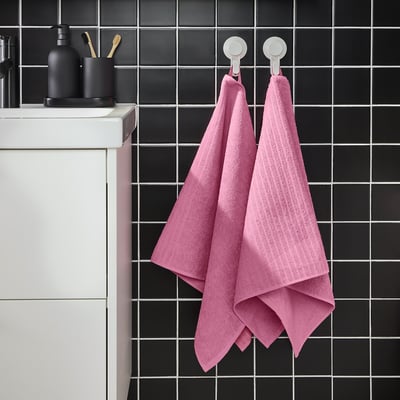 Bright pink VÅGSJÖN towel hangs on black tiled wall. Medium thickness, cotton. Two hooks, large.