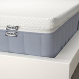 Close-up of a white mattress with blue ikea tags on a white bed frame, showcasing its quality.