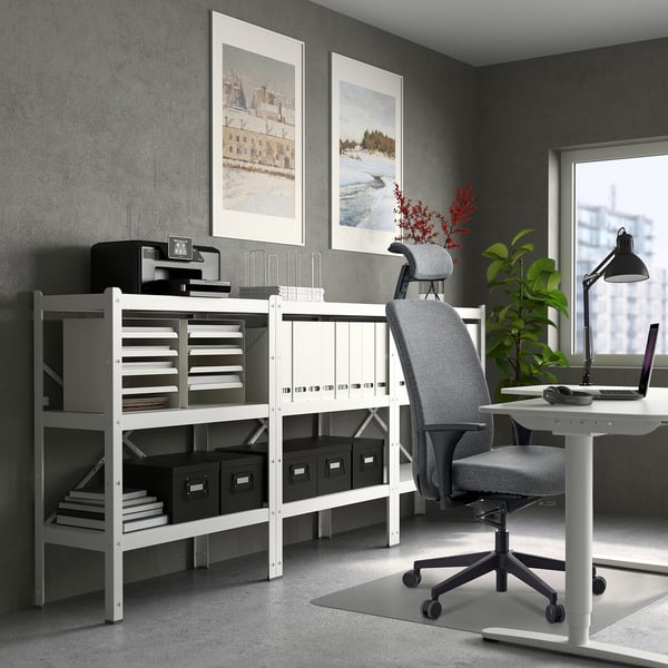 Modern home office with white desk, grey ergonomic chair, shelves, & laptop.