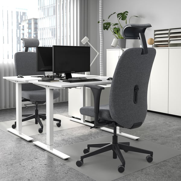Modern office desk with dual screens, 2 ergonomic chairs, white cabinet, plant.
