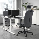 Modern office desk with dual screens, 2 ergonomic chairs, white cabinet, plant.
