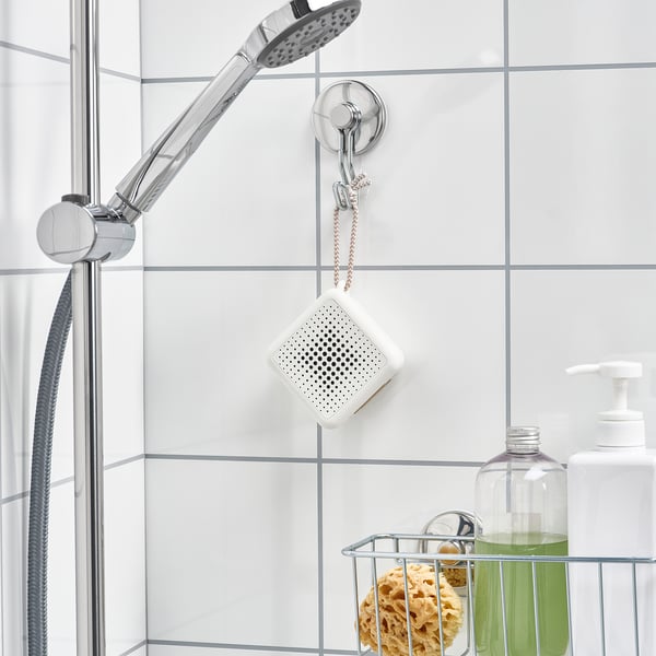 Portable waterproof speaker hangs in bathroom, playing music near shower.