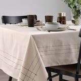Table set with beige VÅRARV cloth, plates, bowls, glasses, cutlery, and chairs, ideal for seating 4-6 people.