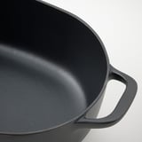 Close-up of black enameled cast iron pan handle, smooth and sturdy, highlighting durable quality.