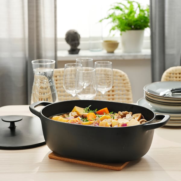 Cast iron casserole with veggies and wine on wooden table.