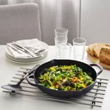 Cast iron skillet with stir-fried vegetables on a trivet, plates, napkins, and cups nearby.