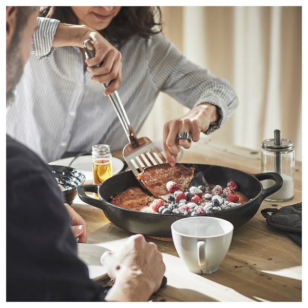 A person serves food from a black cast iron skillet filled with bread and berries onto a plate.