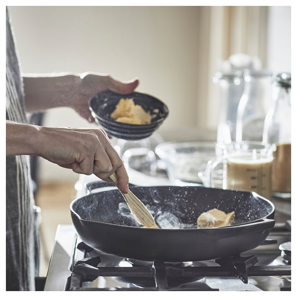 Cooking scene: two hands stiring butter in a black cast-iron pan on a stove, with a bowl of flour nearby.