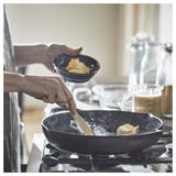 Cooking scene: two hands stiring butter in a black cast-iron pan on a stove, with a bowl of flour nearby.